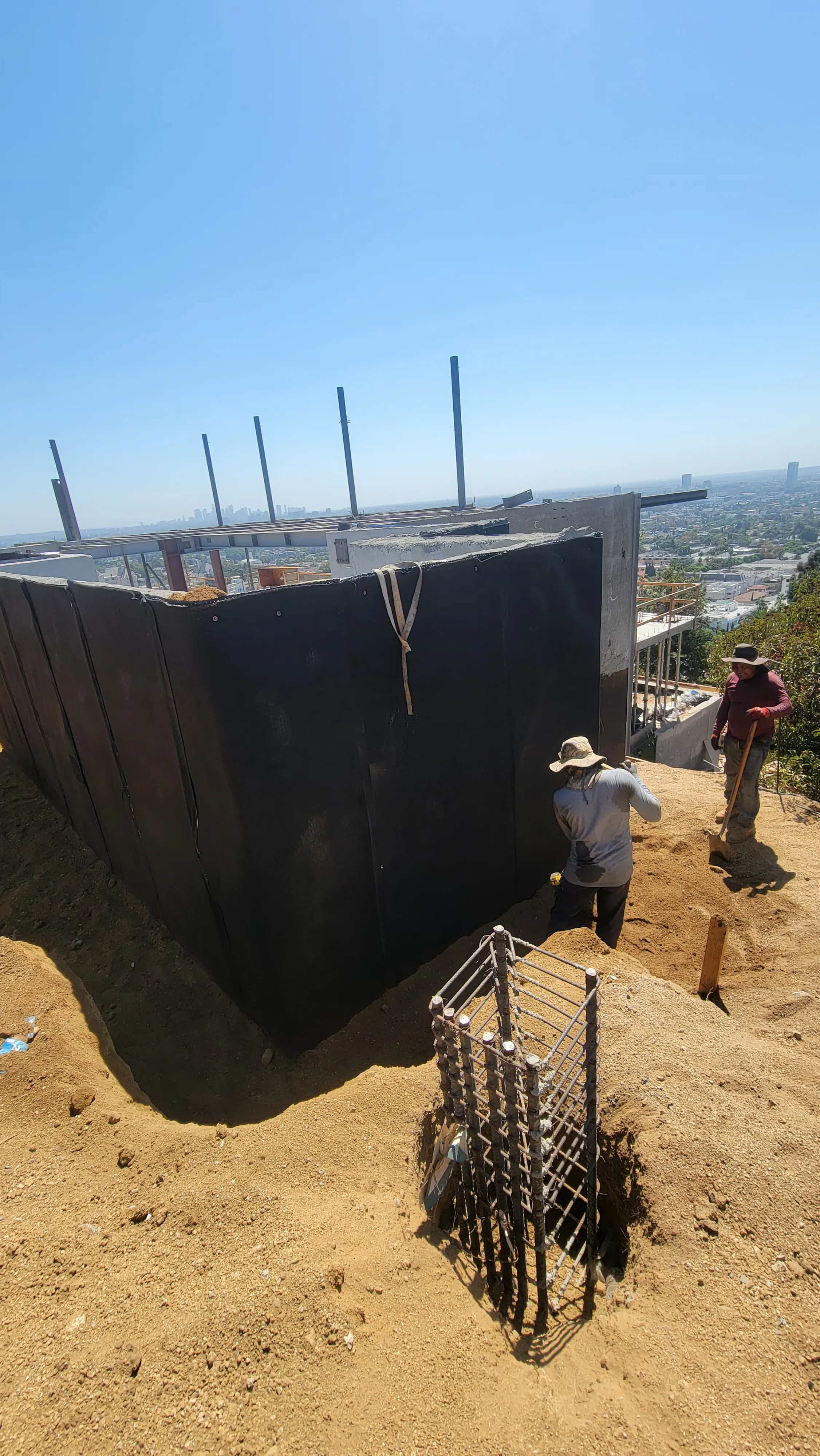 Exterior foundation wall being waterproofed with elastomeric liquid membrane and drainage matting.